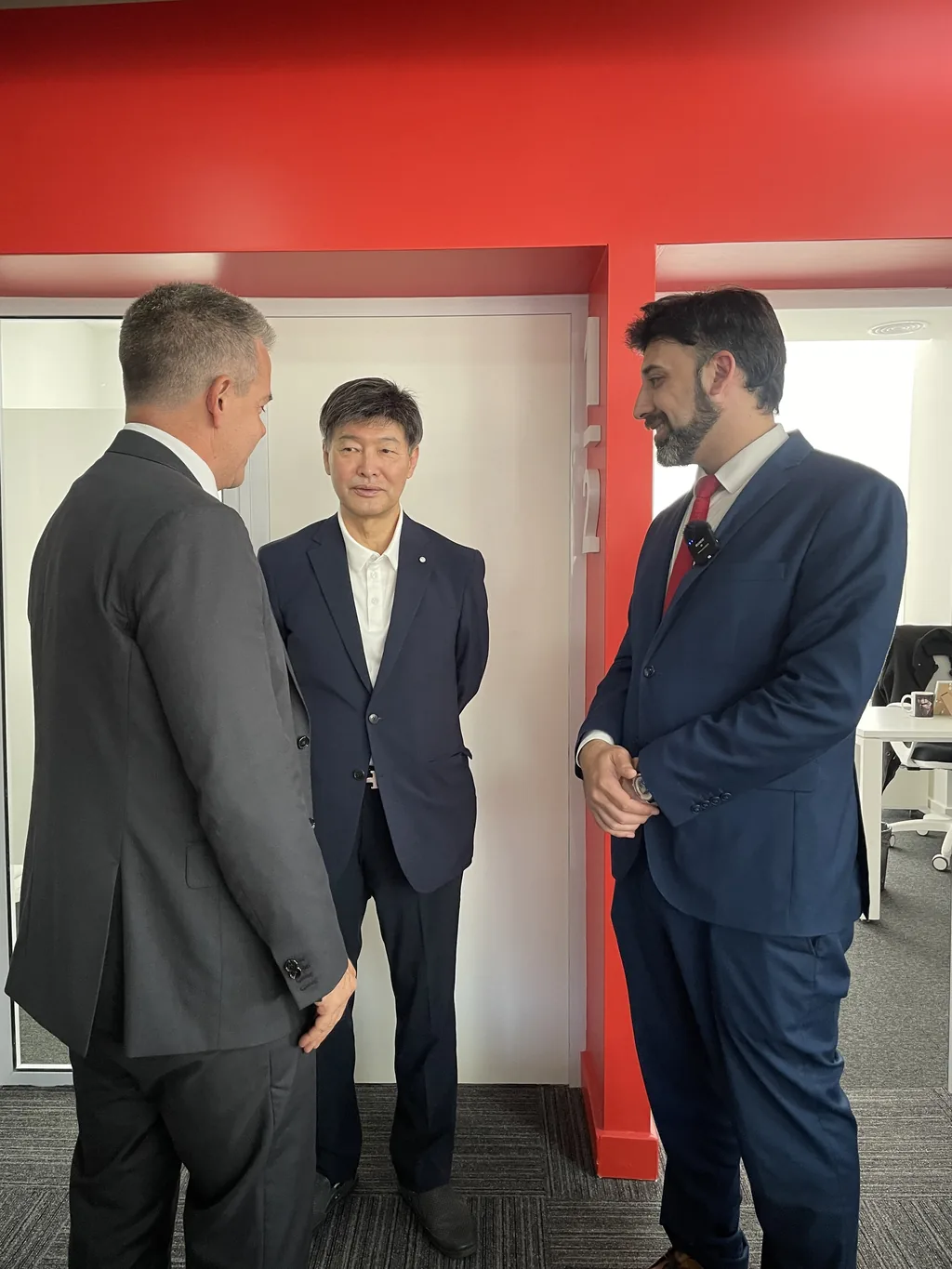 Tres participantes intercambian ideas junto a una sala vidriada durante la visita institucional de G-CERTI.