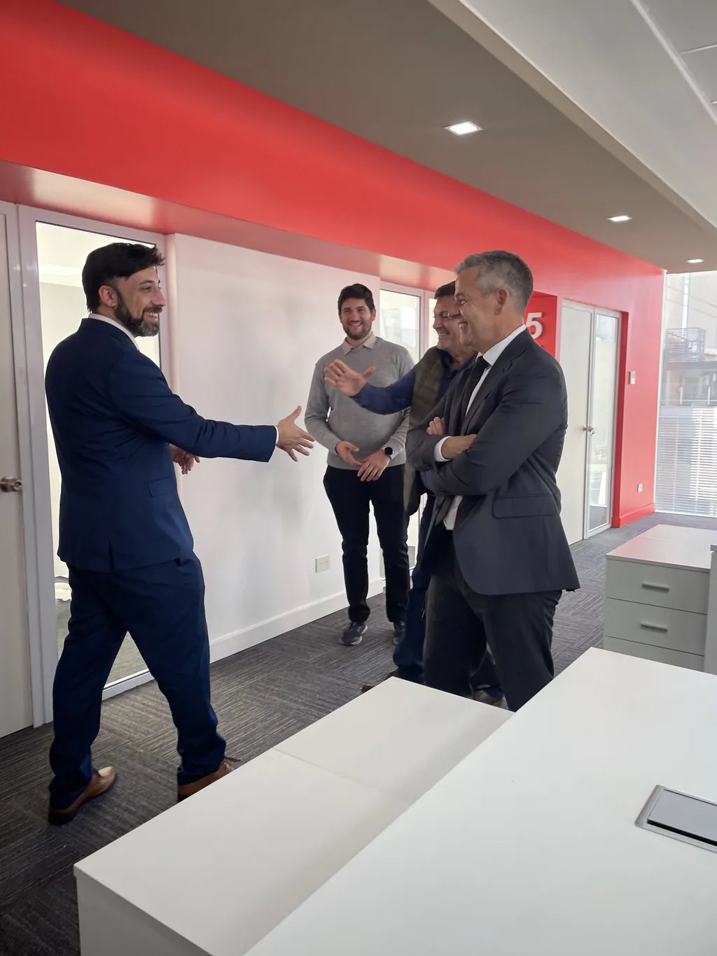 Cuatro participantes conversan en el pasillo de una oficina durante una visita institucional de G-CERTI.