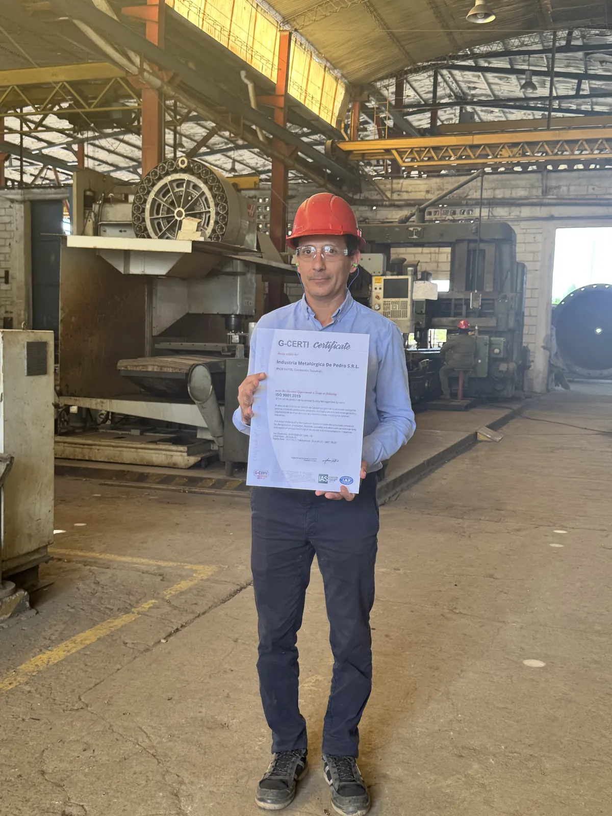 Person wearing a hard hat holds a certificate at a plant